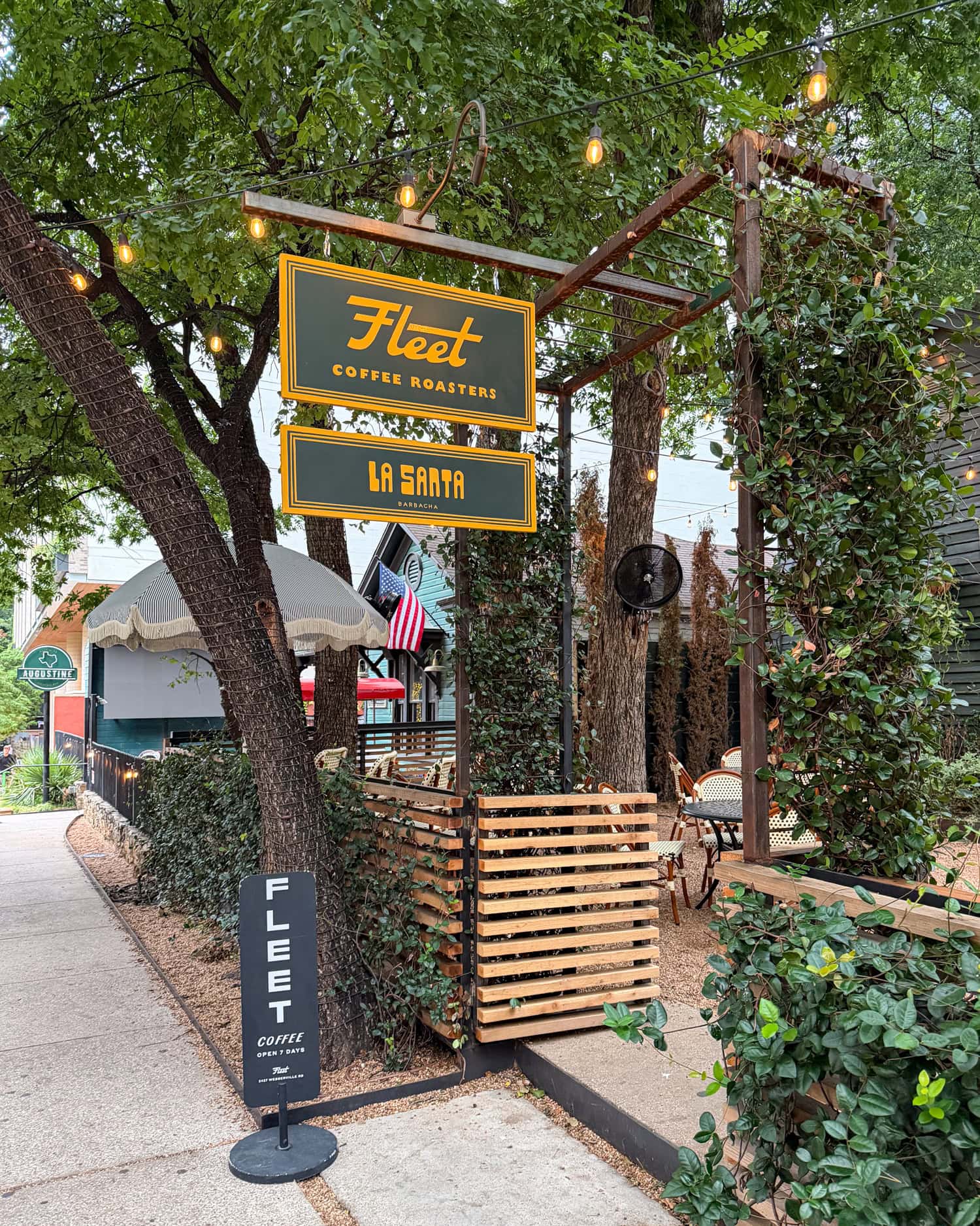 Fleet Coffee and La Santa Barbacha signs outside their shared, tree-shaded patio on Rainey Street in Austin