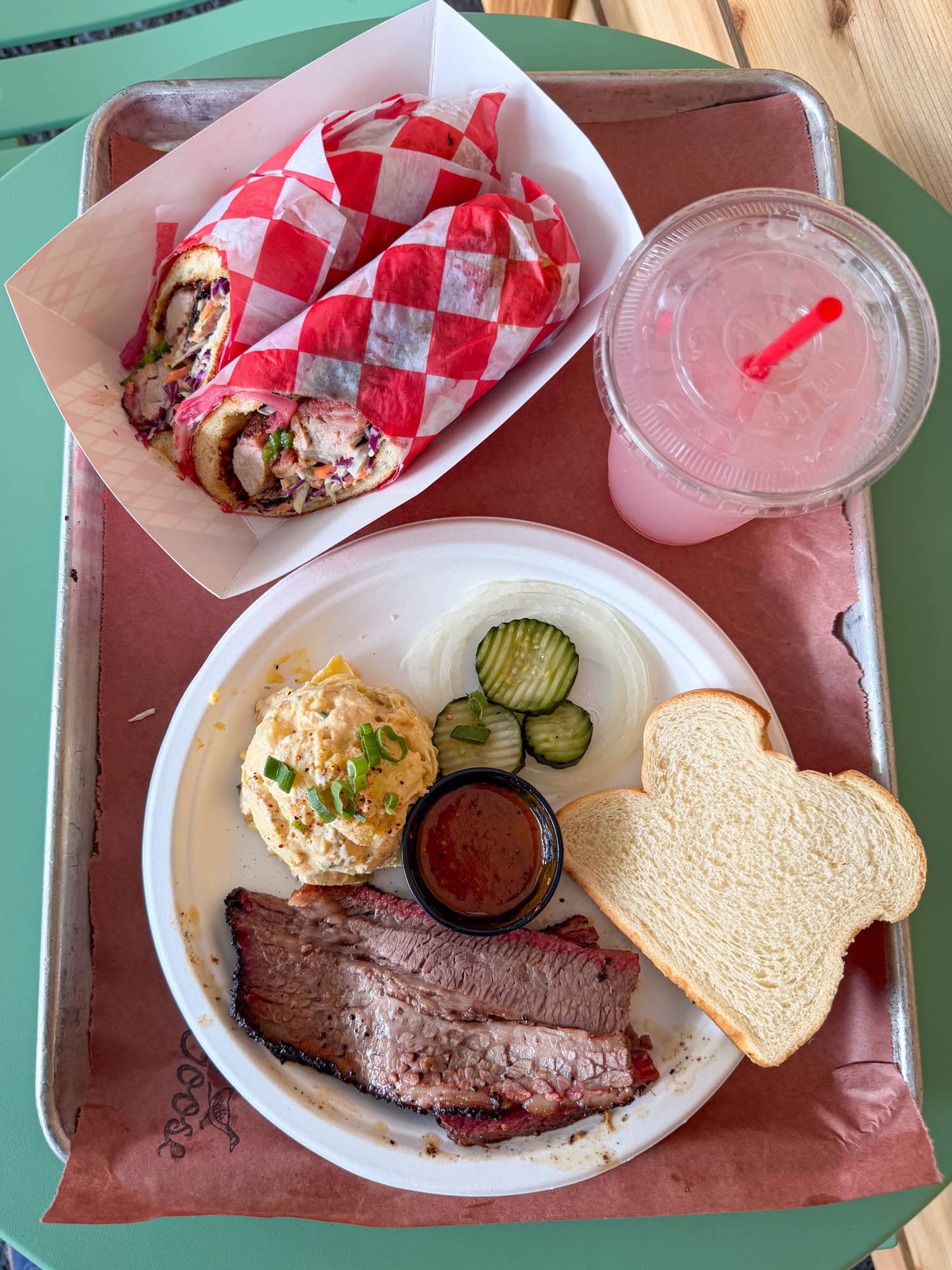 Flat lay of brisket, potato salad, Goose Juice lemonade, and a pork belly bánh mì at Two Goose barbecue in Austin