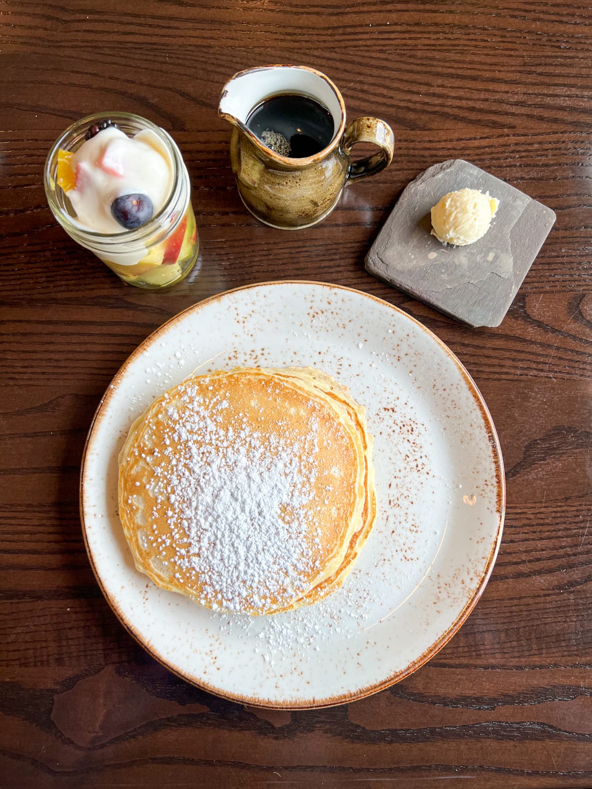 Pancakes, maple syrup, and a side of fruit with yogurt