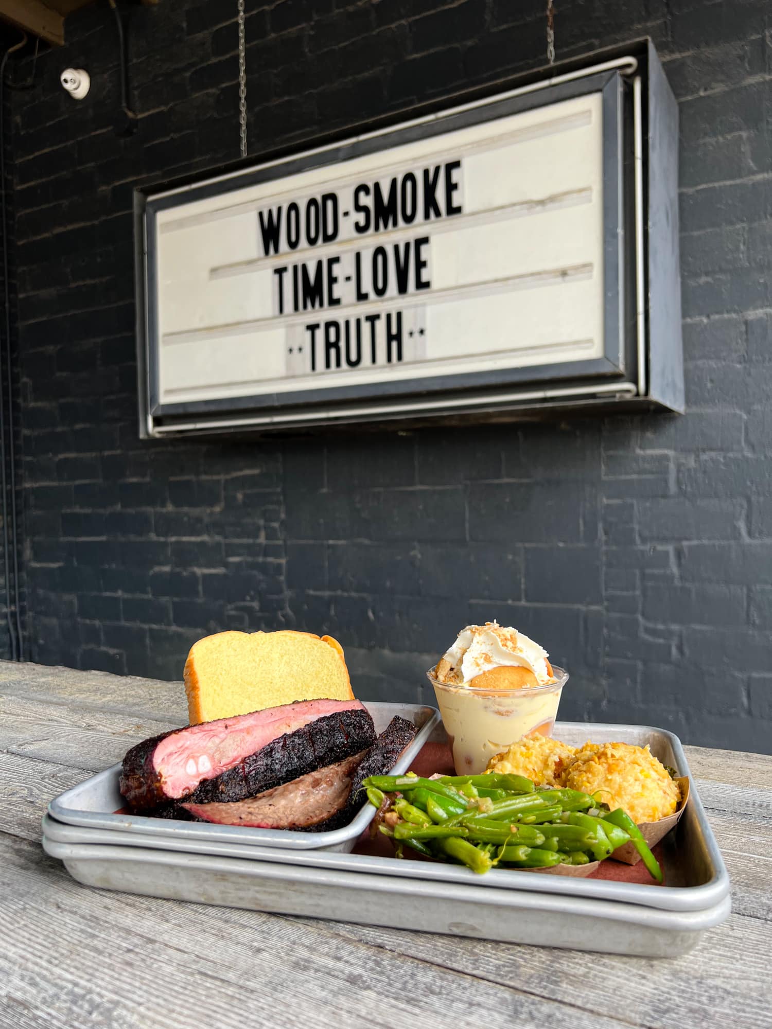 Brisket and pork ribs with a sign that says "wood, smoke, time, love" — Truth