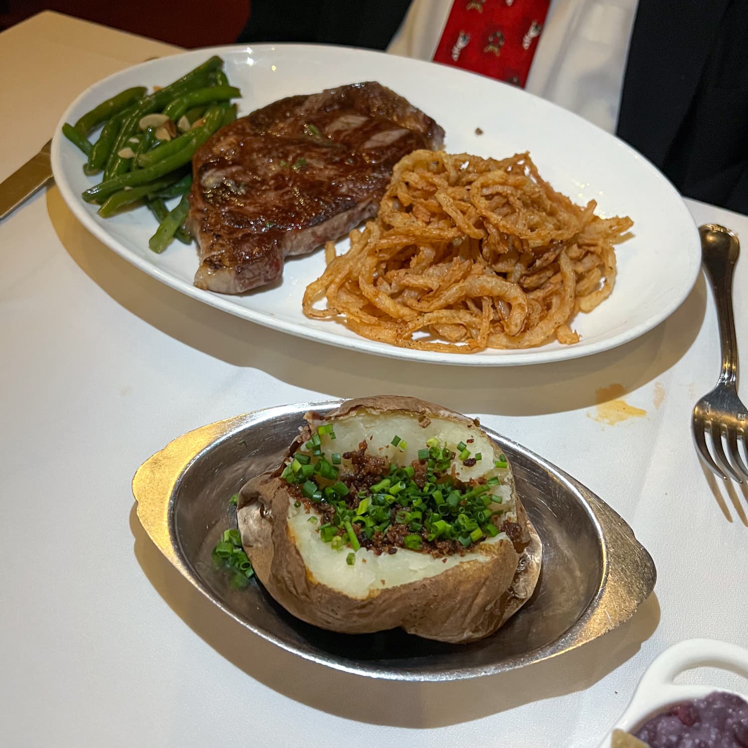 A 14-ounce Delmonico steak with string beans, onion rings, and baked potato 