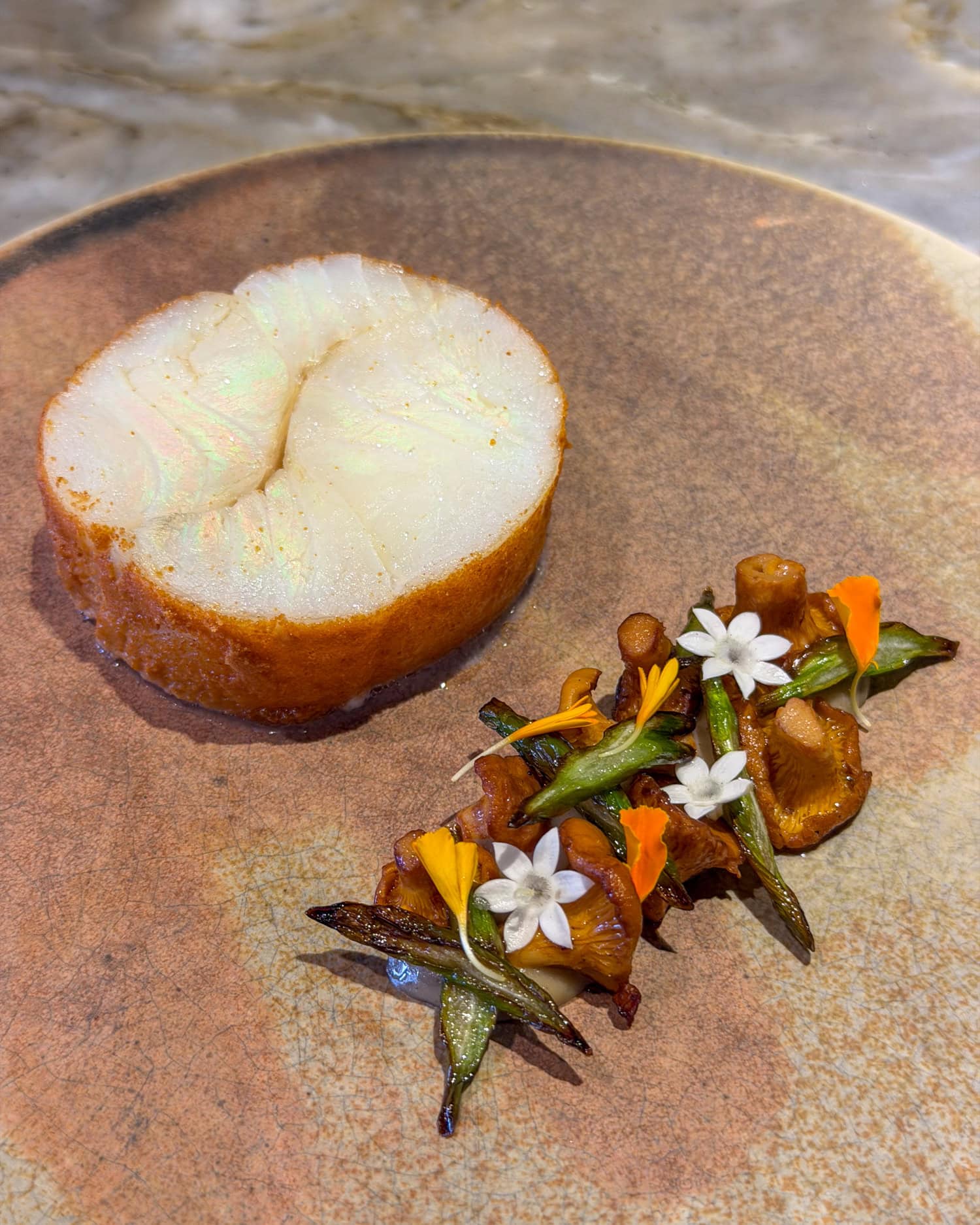 Cod with St. George mushrooms, asparagus, and edible flowers on a ceramic plate at EBBE in Tampa.