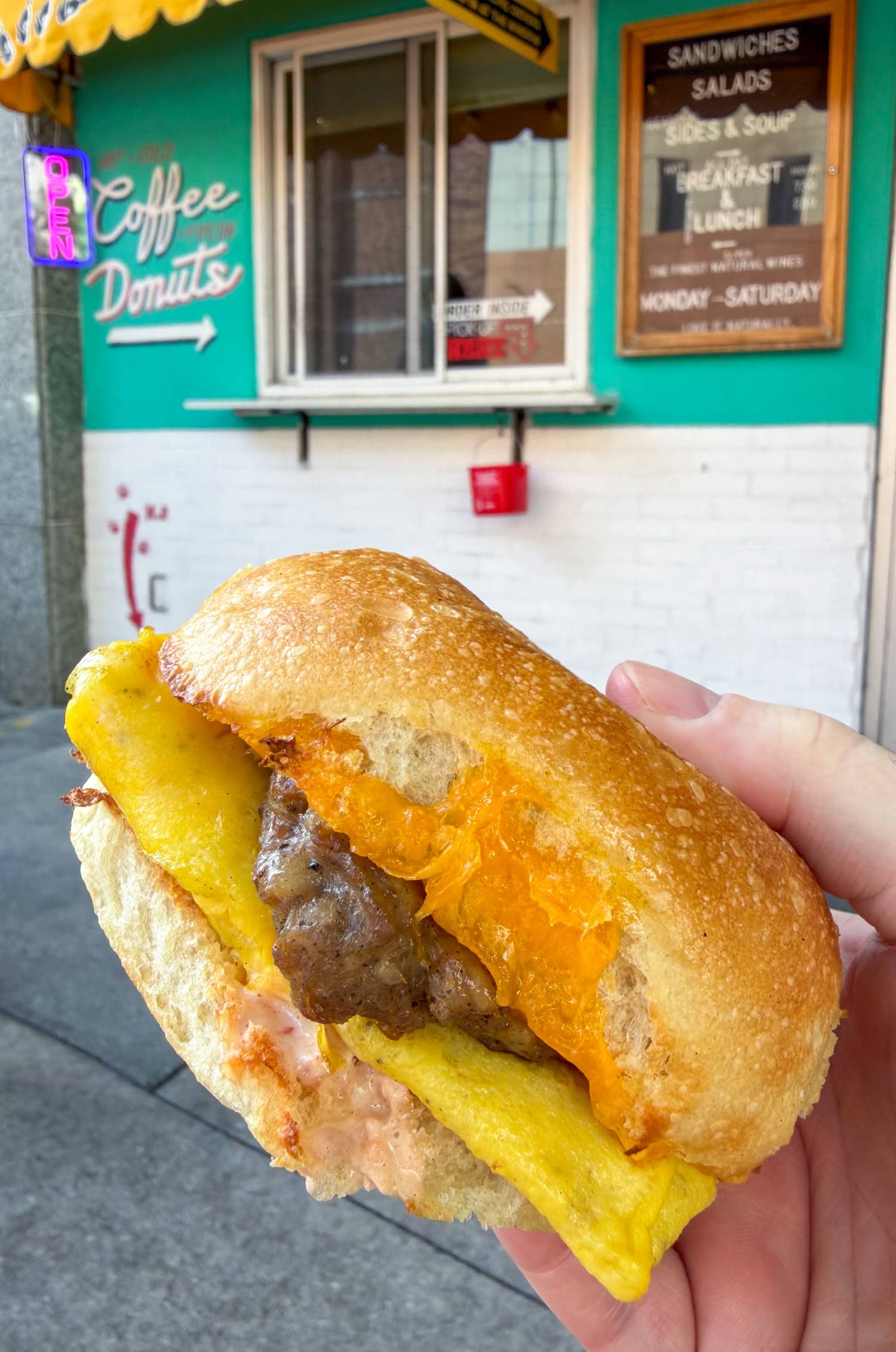 Sausage, egg, and cheese sandwich held in front of SuperNatural Food & Wine's downtown Tampa storefront.