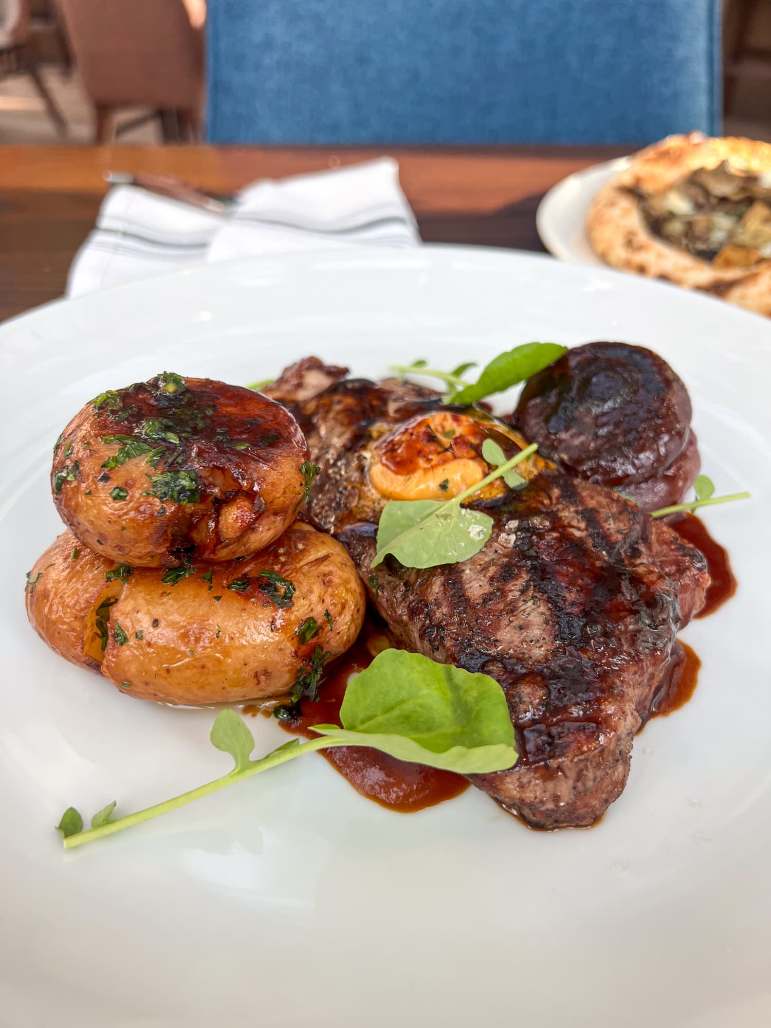 10-ounce New York strip steak with cipollini onions, watercress, chipotle-garlic compound butter, fingerling potatoes, and red wine demi-glace