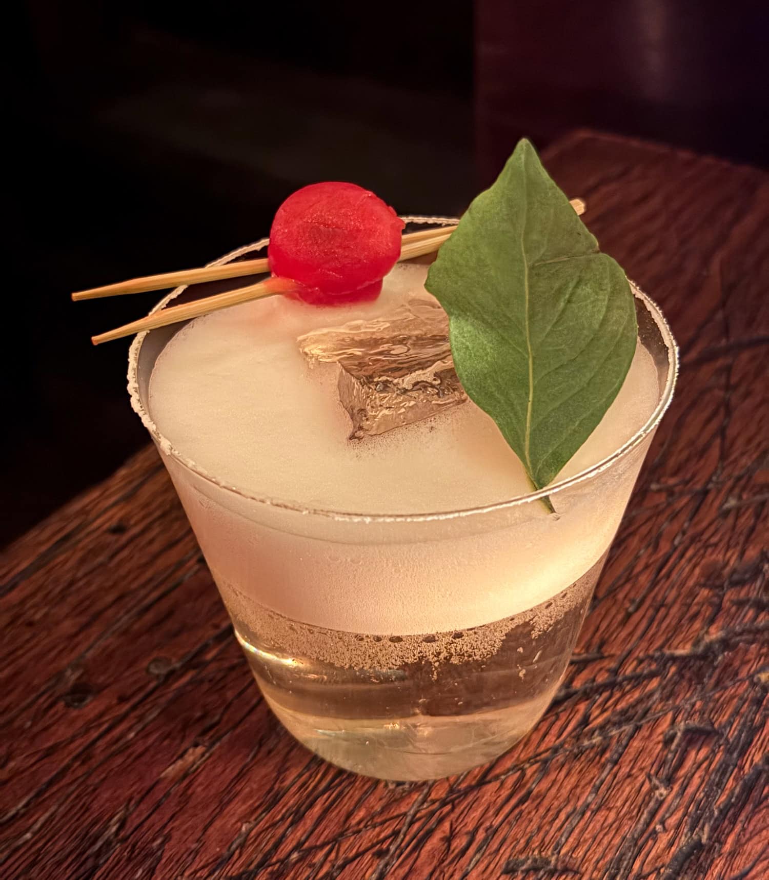 Tomato Tree cocktail with a large green leaf and red tomato garnish at Sip & Guzzle in New York City.