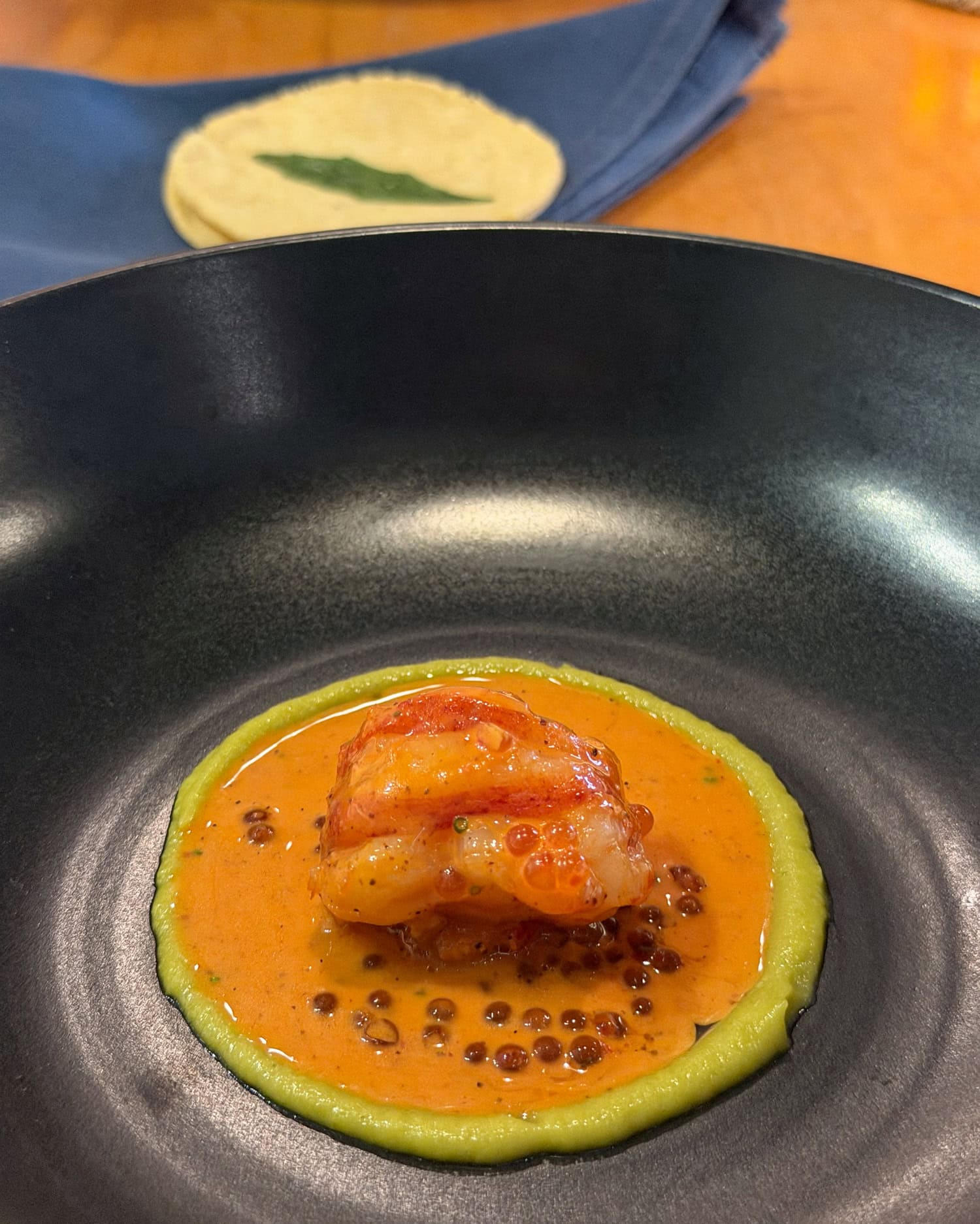 Lobster al pastor in orange sauce inside a green purée ring, with corn tortillas behind the black bowl at Mixtli.