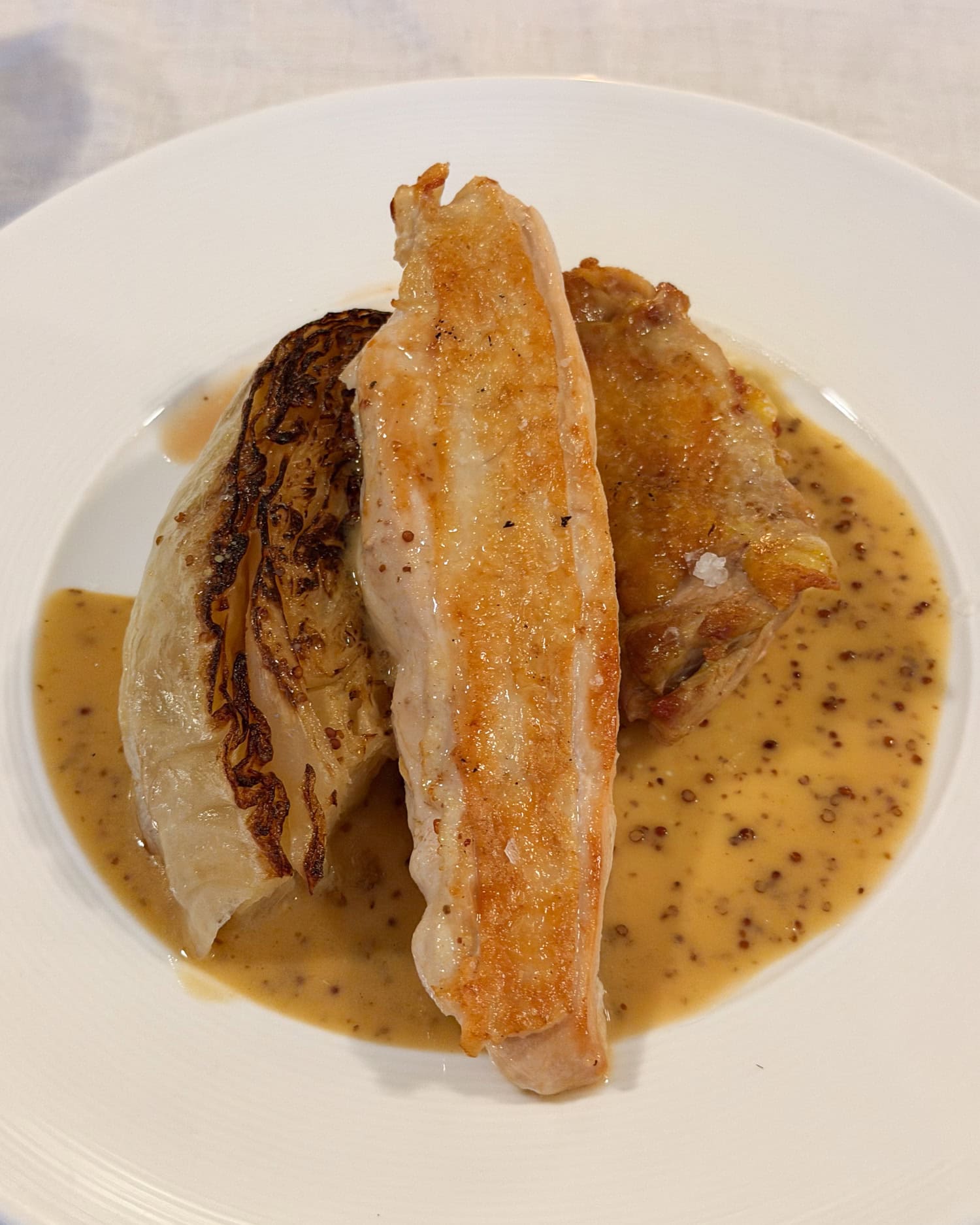 Golden-skinned chicken beside a charred cabbage wedge in sauce on a white plate at Petit Coquin.