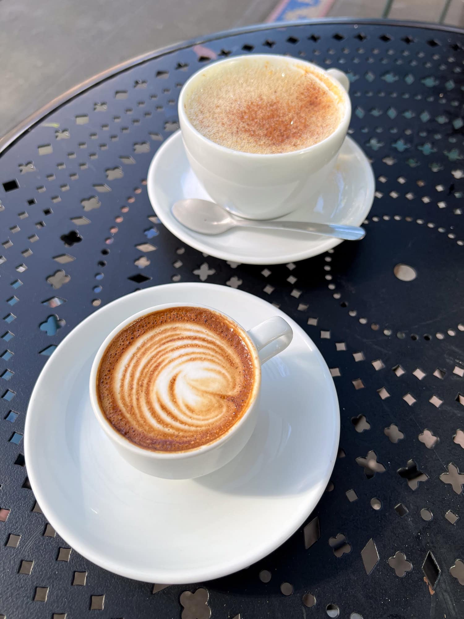 A macchiato and a hot cider at an outdoor cafe table.