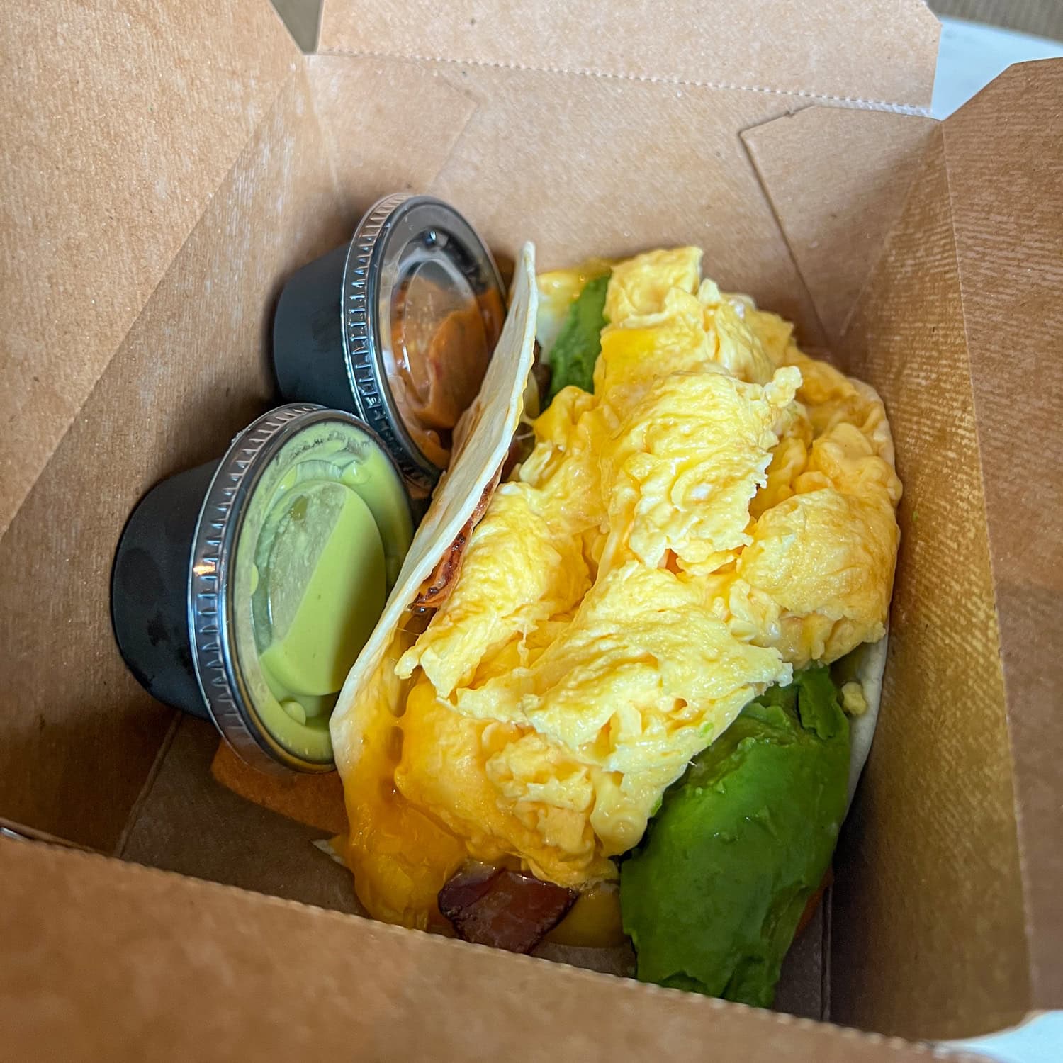 A giant bacon, egg, cheese, and avocado breakfast taco served with red and green salsas.