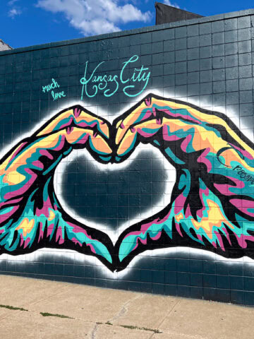 Mural in Kansas City's Crossroads Arts District featuring two hands forming a colorful heart shape and the words "Much Love."