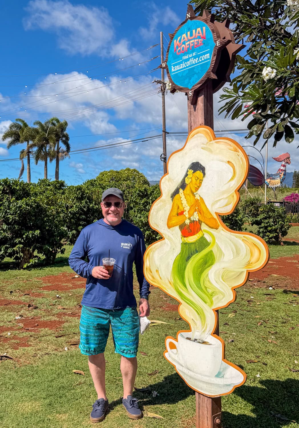 Dave holding iced coffee next to Kauai Coffee Company sign in Koloa