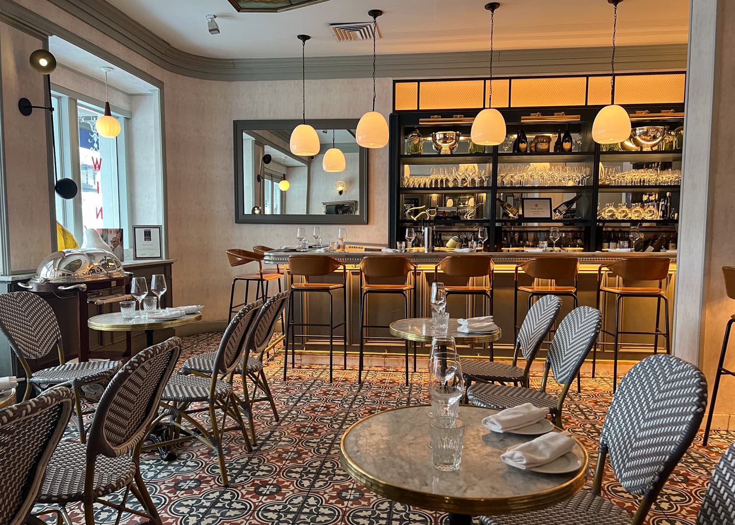 Interior dining room at Benoit restaurant in Midtown Manhattan with marble tables, woven chairs, pendant lights, and a long bar.