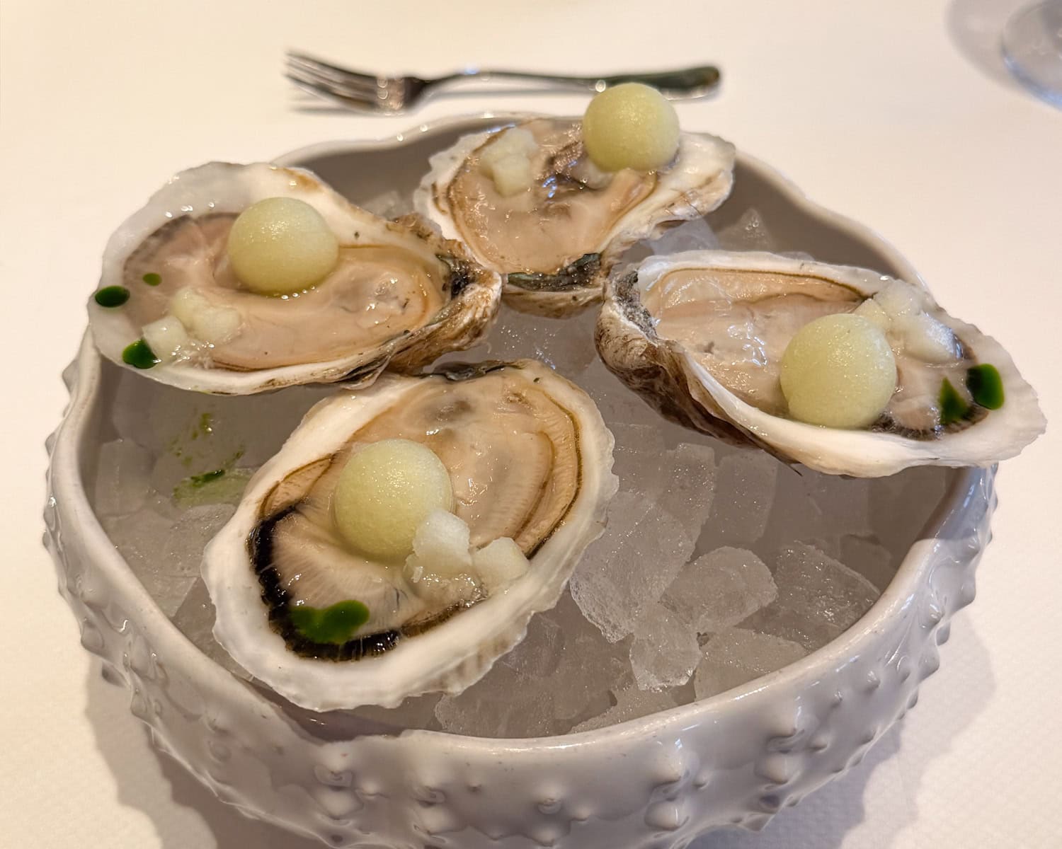 Fresh oysters on ice at Café Carmellini in New York City topped with melon pearls and served in a white ceramic bowl.