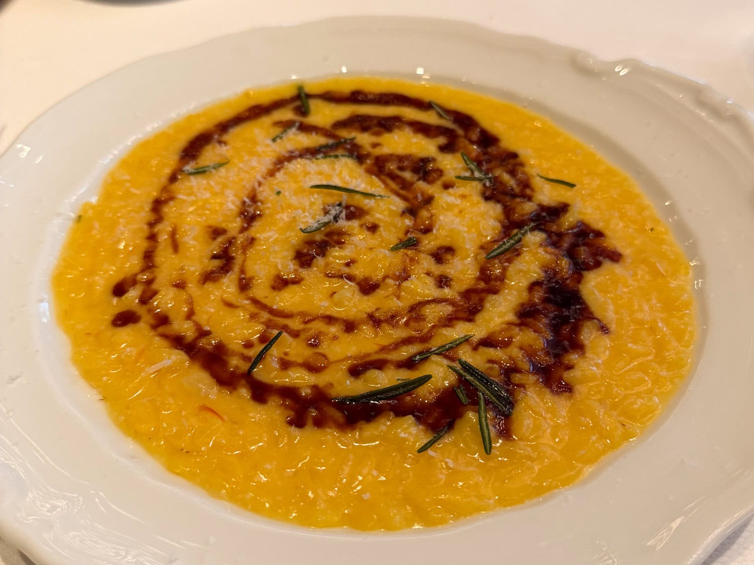 Saffron risotto at Café Carmellini in New York City topped with rosemary and a dark sauce swirl on a white plate.