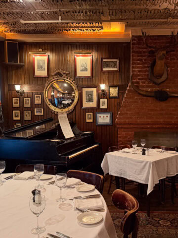 Historic dining room with piano, fireplace, and framed portraits at Keens Steakhouse in NYC.