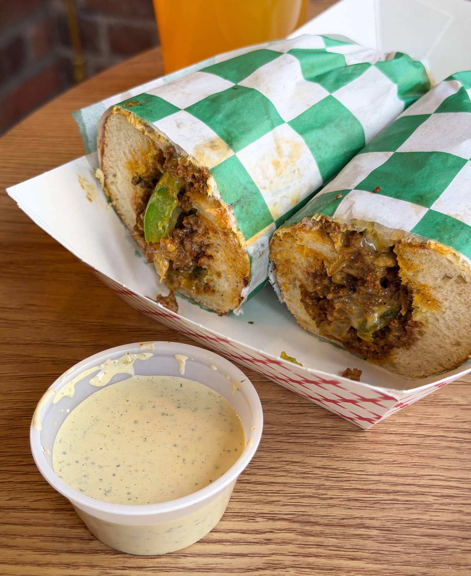Chopped cheese sandwich at Nishaan in New York City served with dipping sauce on a wooden table.