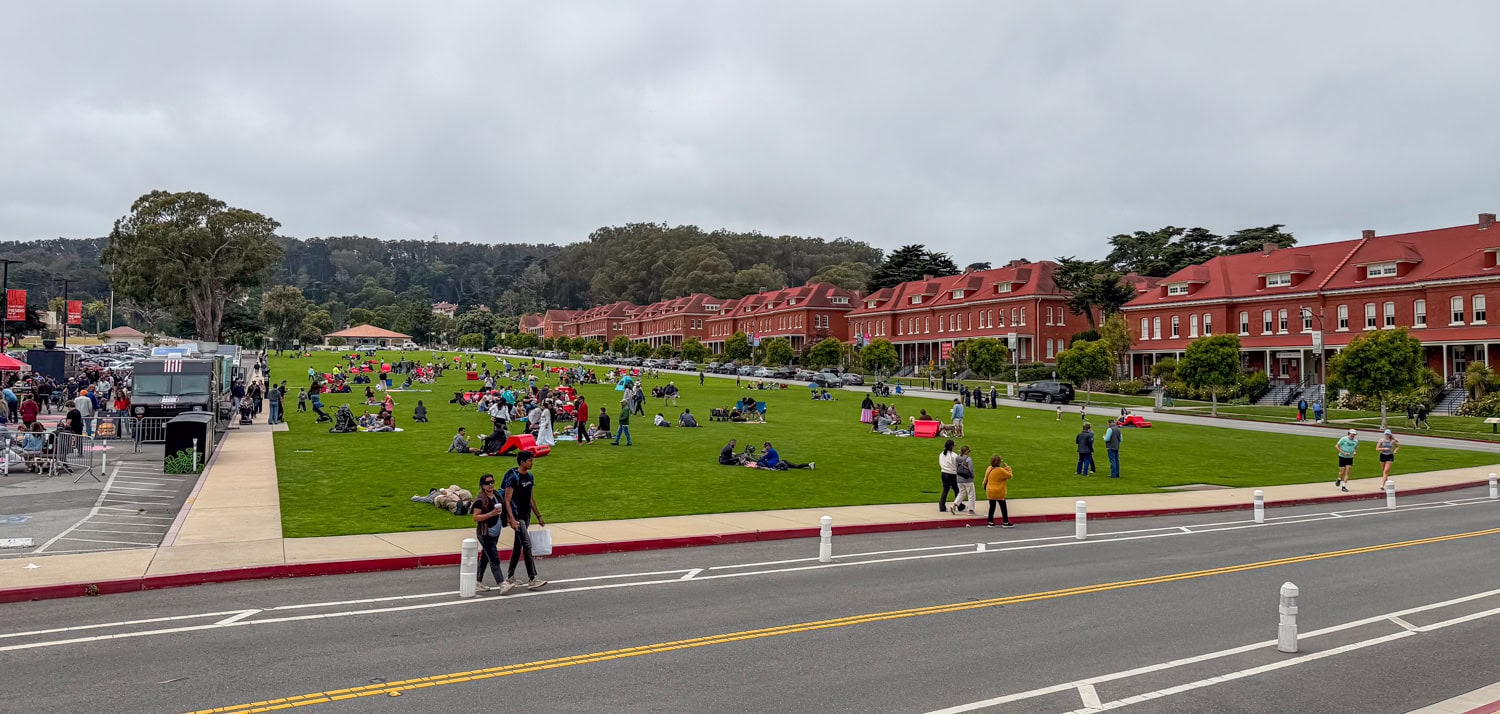 Families picnicking on the Presidio's Main Parade Lawn beside food trucks and historic red-brick buildings