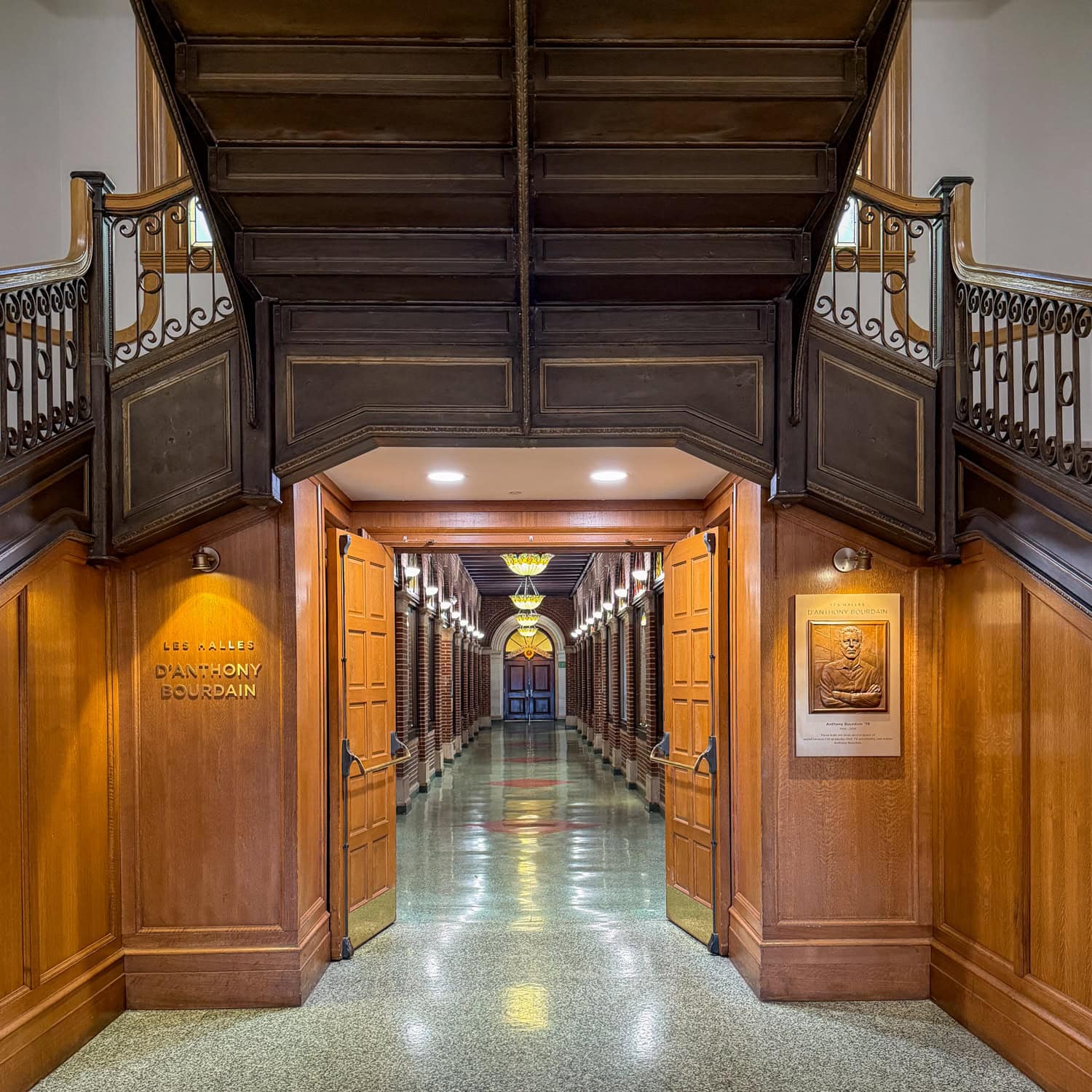 Entrance to Les Halles d'Anthony Bourdain with a commemorative plaque and a long brick hallway beyond open wooden doors.