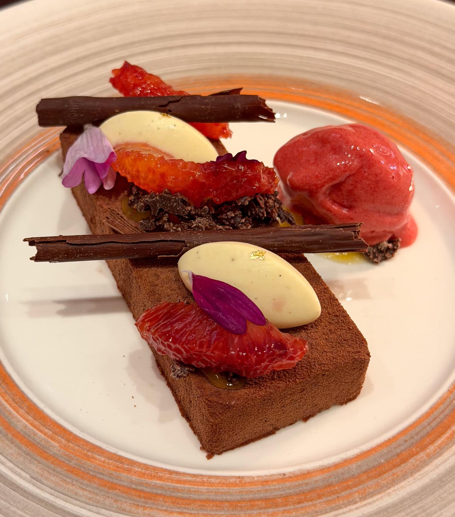Dark chocolate dessert with vanilla Bavarian cream, blood-orange segments, edible flowers, chocolate shards, and red sorbet while dining at the Culinary Institute of America.