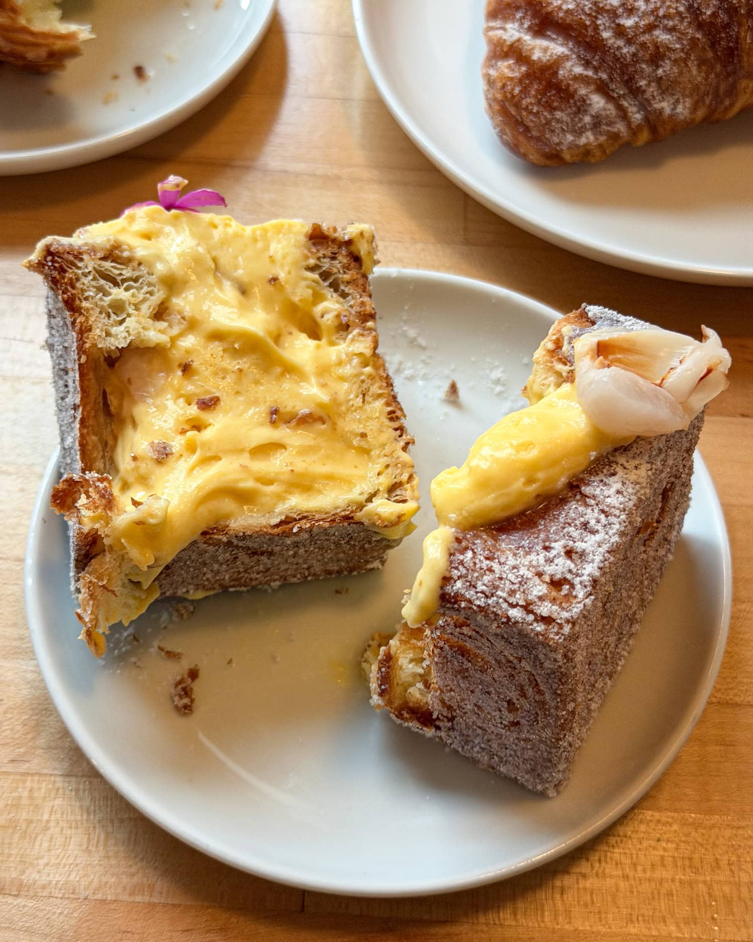 Cut-open cube-shaped croissant showing laminated pastry layers and yellow mango, passion fruit, and lychee filling.