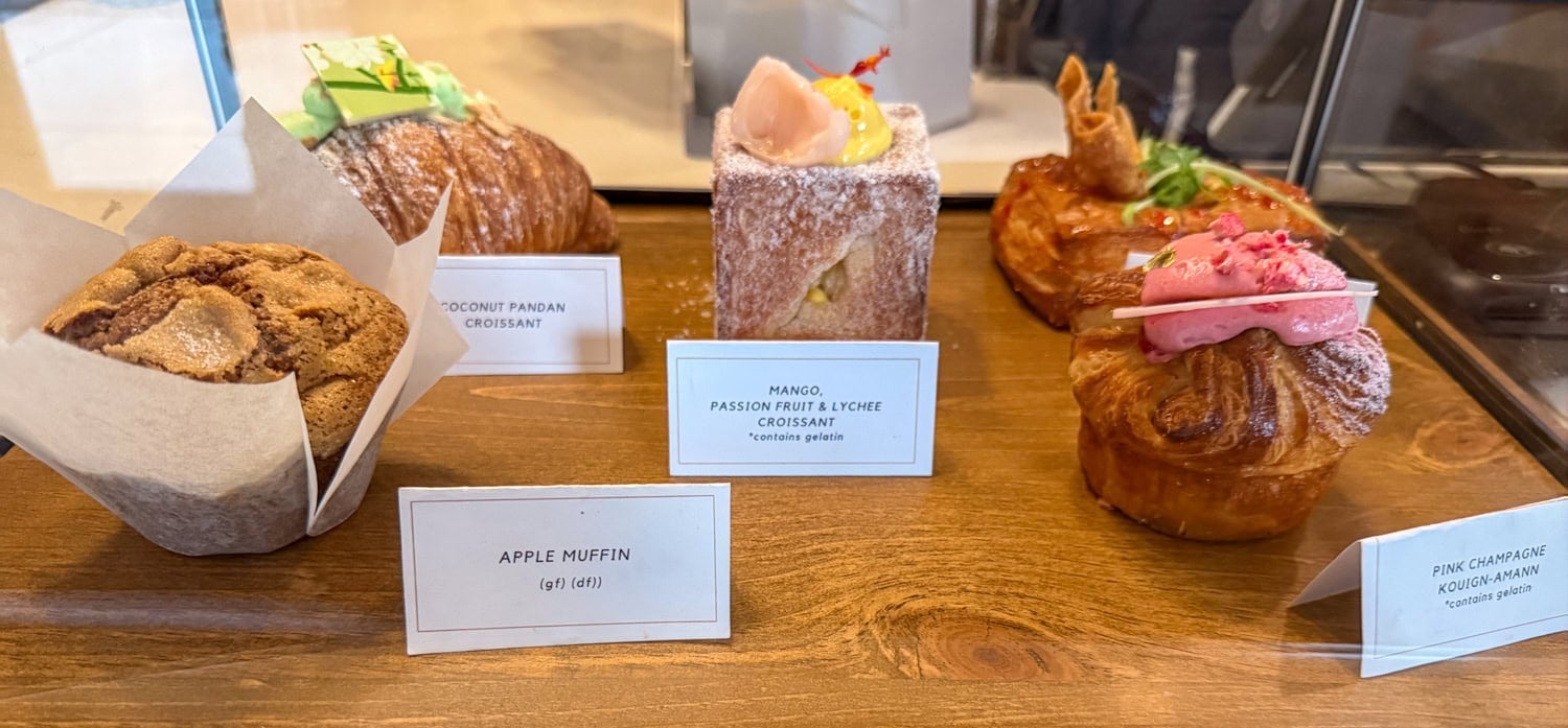 Pastry case displaying coconut pandan and mango, passion fruit, and lychee croissants alongside other pastries.