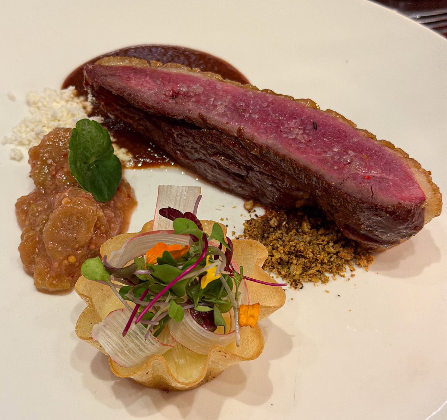Sliced pink duck breast with rhubarb compote, sauce, microgreens, and vegetables in a crisp tart shell.