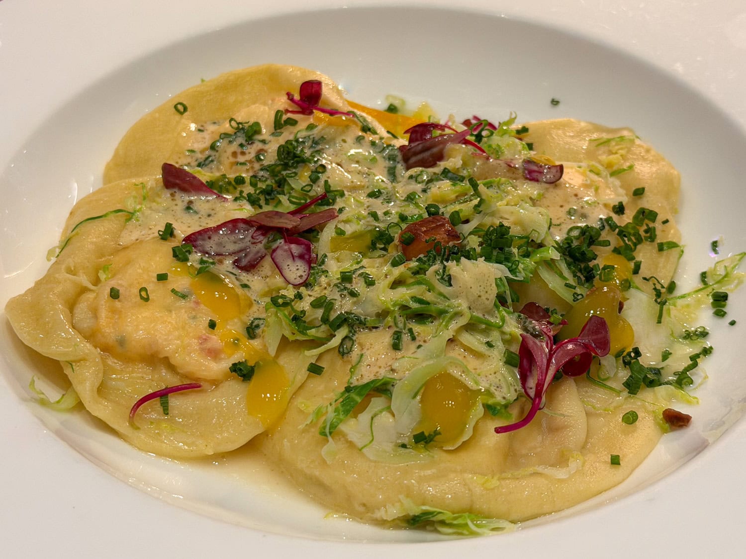 Lobster ravioli topped with shredded Brussels sprouts, herbs, purple leaves, and creamy lobster sabayon.