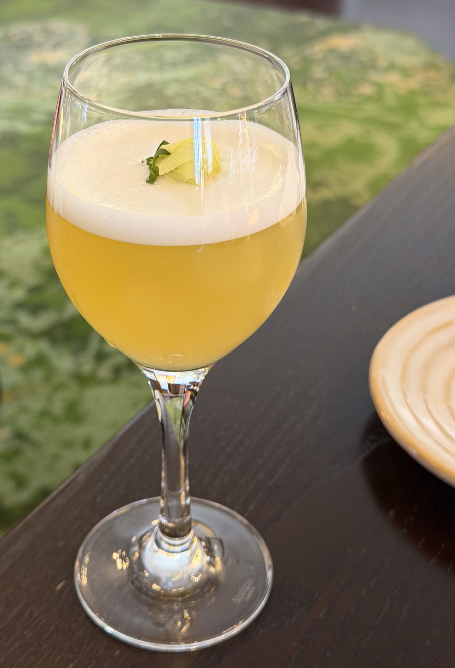 Pale yellow Mother's Bloom gin cocktail topped with foam and a flower garnish at American Bounty Restaurant.