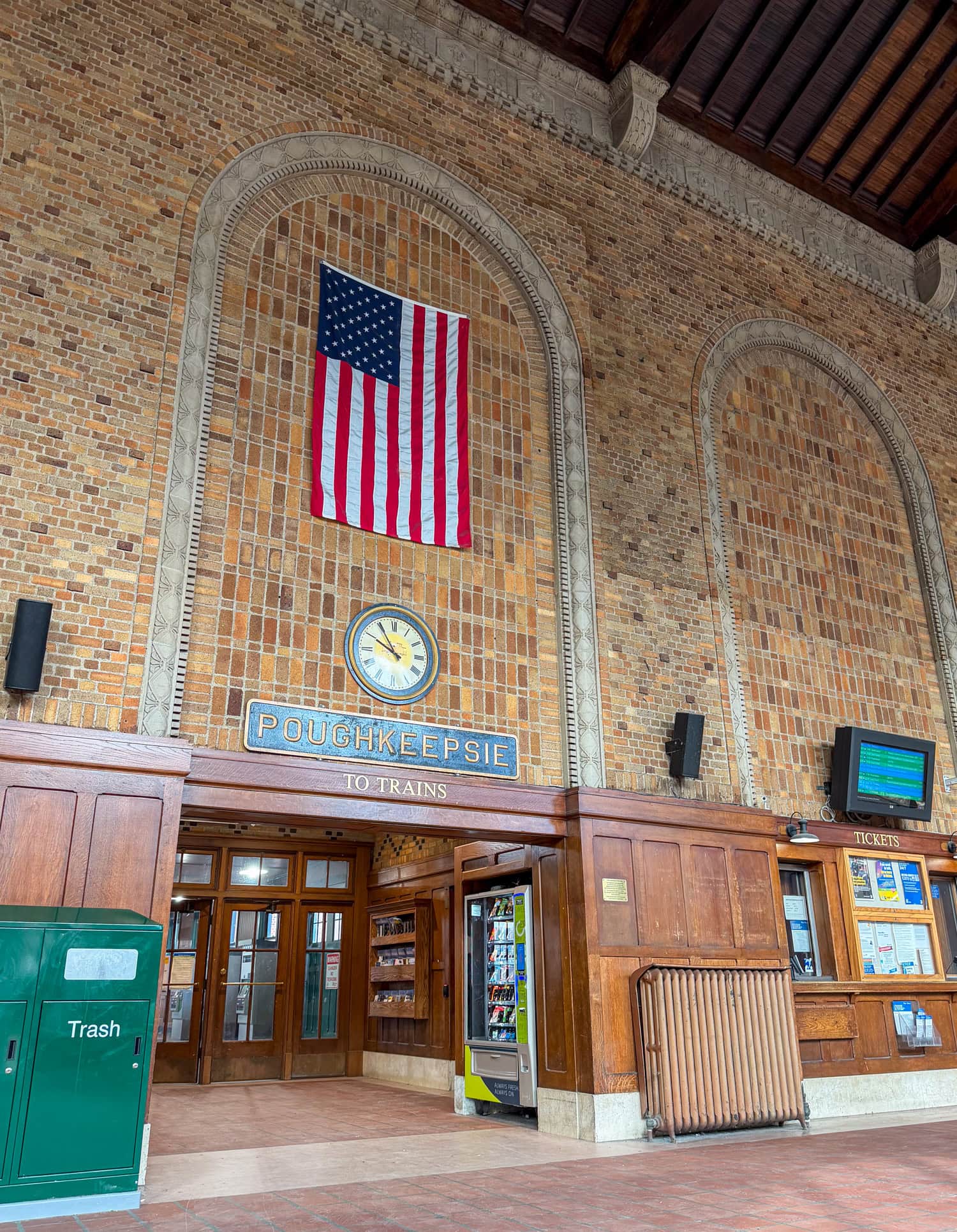 Interior of the Poughkeepsie train station with an American flag, clock, and station sign.