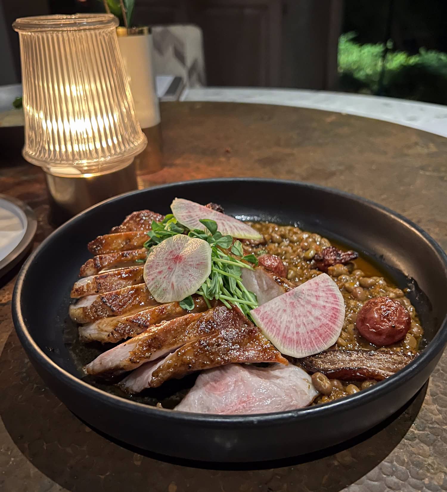Sliced Berkshire pork chop with field peas, pink radish slices, and pea tendrils in a black bowl at Arlo Grey.