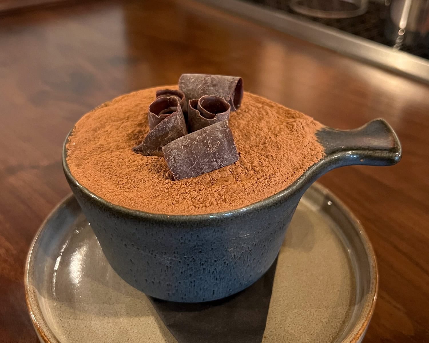 Irish coffee tiramisu dusted with cocoa and topped with chocolate curls in a dark handled bowl at The Dead Rabbit.