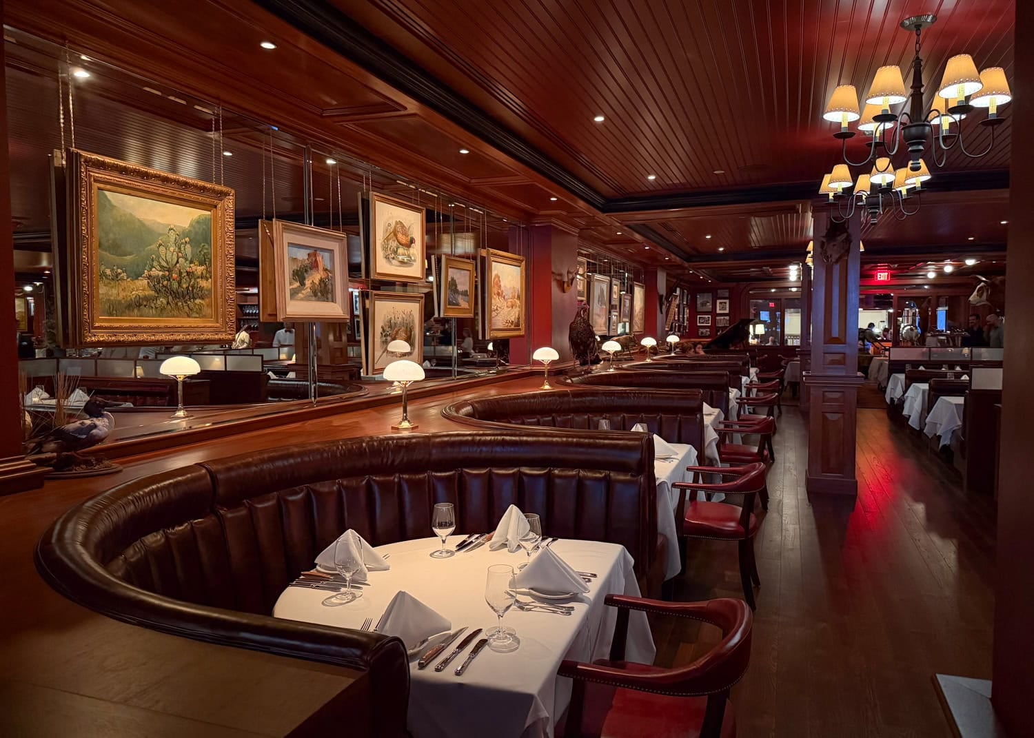 Driskill Grill dining room with curved leather booths, wood-paneled walls, framed paintings, and chandeliers.