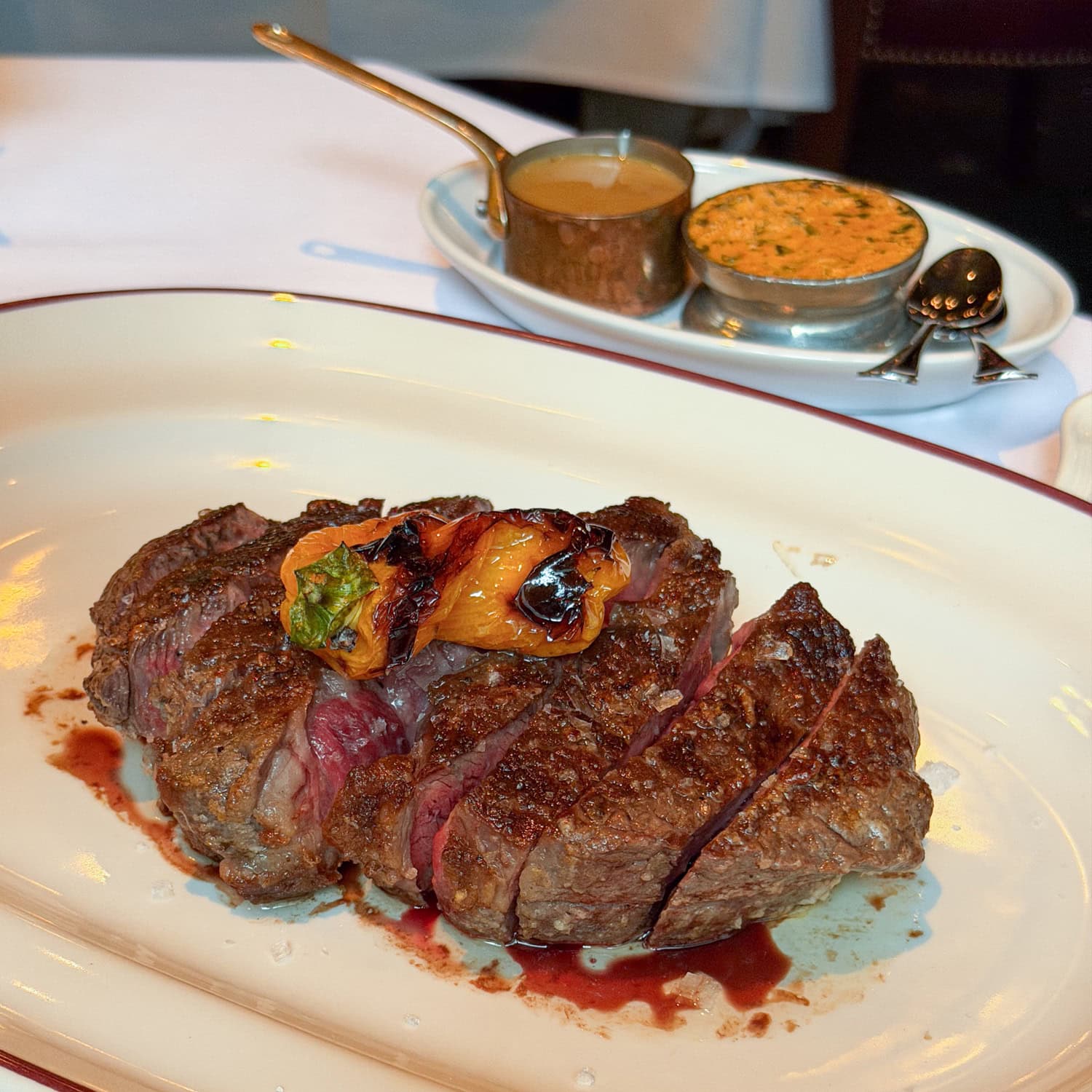 Sliced steak with a browned crust and pink center, topped with blistered peppers on a white platter.