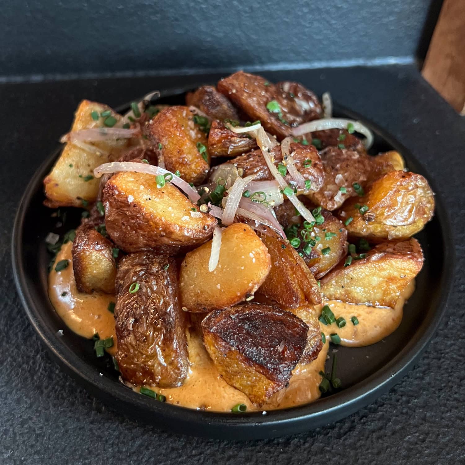Crispy beef fat potatoes with garlic, shallots, and American Wagyu beef tallow on a black plate at Ember Kitchen in downtown Austin.