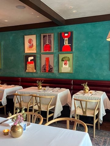 Jeffrey's dining room with teal walls, colorful abstract artwork, white tablecloths, and cream pendant lights.