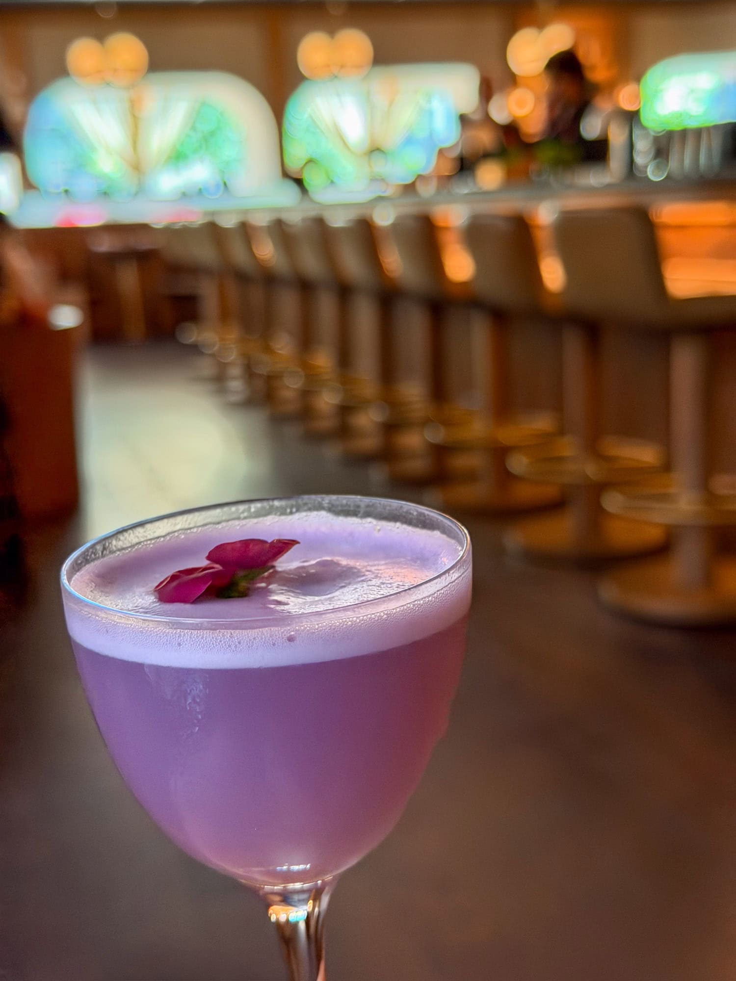 Purple NA cocktail with a foamy top and flower garnish, with Uchibā's bar softly blurred behind it.