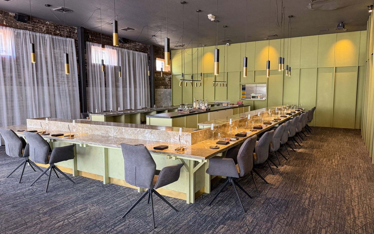 U-shaped marble dining counter with gray chairs, green wall panels, and pendant lights inside EBBE in Tampa.