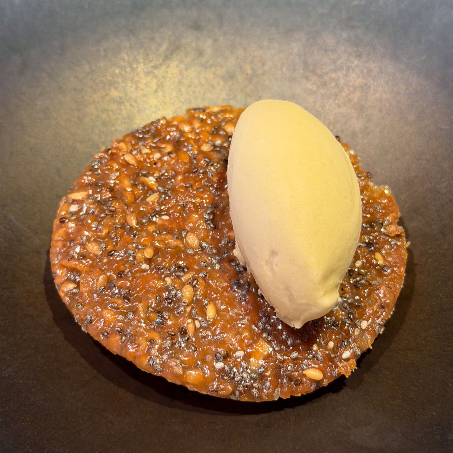 Caramel seed tuile topped with a pale quenelle on a dark plate