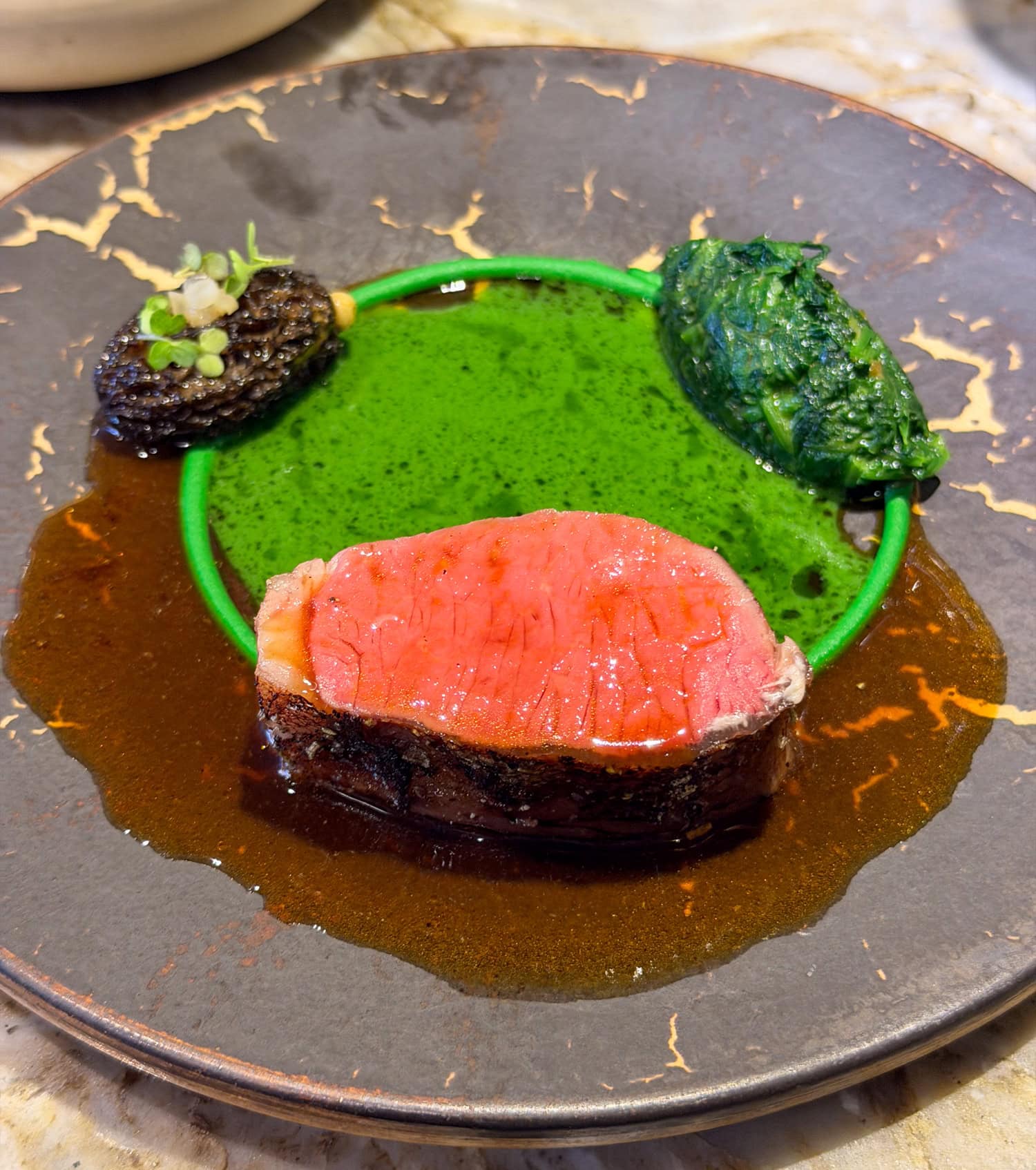 Pink-centered Dorset lamb with green pea purée, a morel mushroom, and brown sauce on a dark plate at EBBE Tampa.