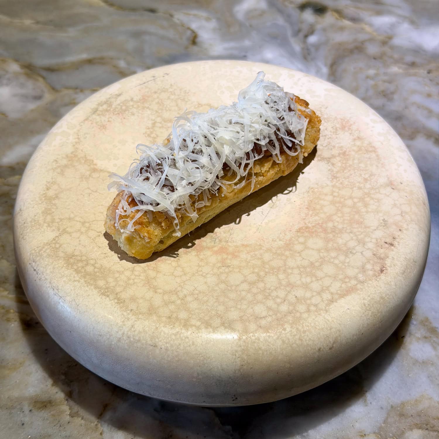 Savory éclair topped with caramelized onion and fine Havgus cheese shavings on a cream-colored plate at EBBE.